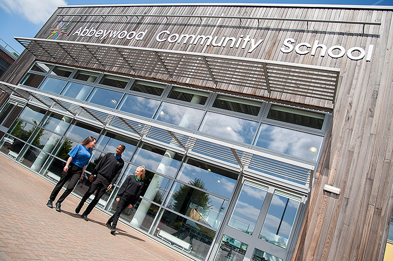 Photo of three students walking in front of the main entrance of Abbeywood Community School.