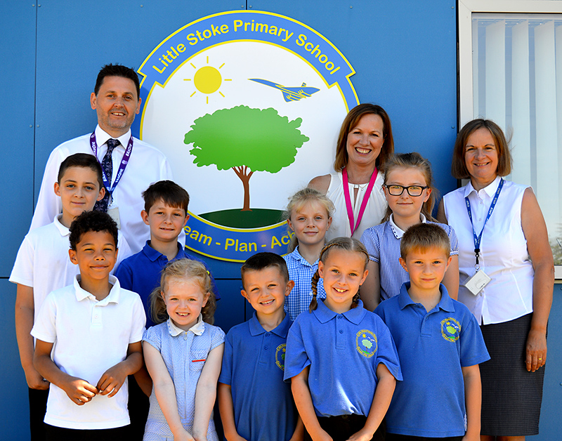 Photo of staff and pupils at Little Stoke Primary School standing in front of a sign depicting the school logo.