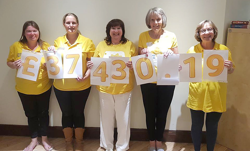 Photo showing members of the Marie Curie Five Stokes Fundraising Group holding up cards showing the amount they have raised since 2014.