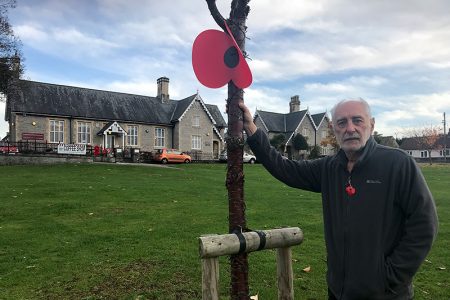 Photo of Adrian Kerton with one of the giant Remembrance poppies he installed.