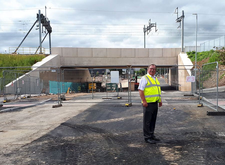 Photo of a man in hi-vis vest standing in front of a bridge.