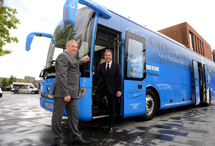 Photo of two men standing near the door of a blue coach.