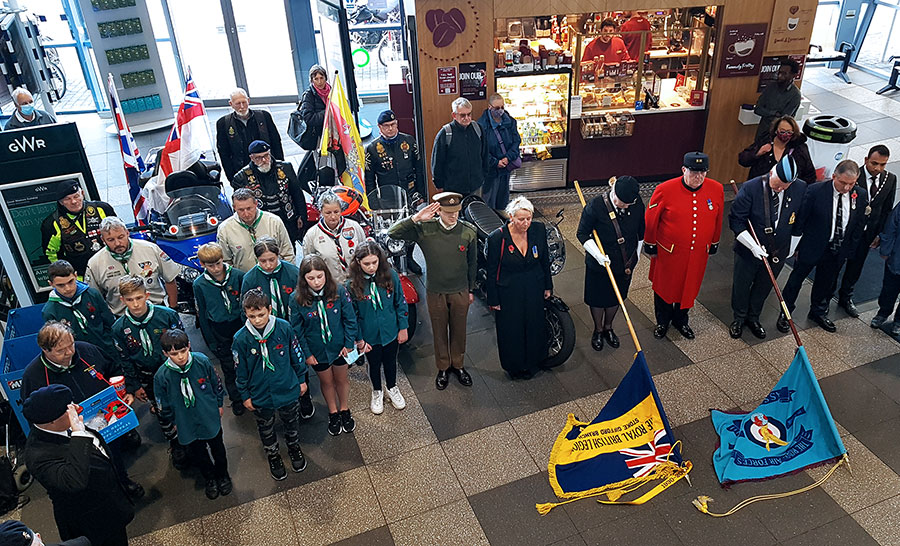Sounding of the Last Post and one minute's silence. Photo of a large group of people standing around two lowered RBL standards.