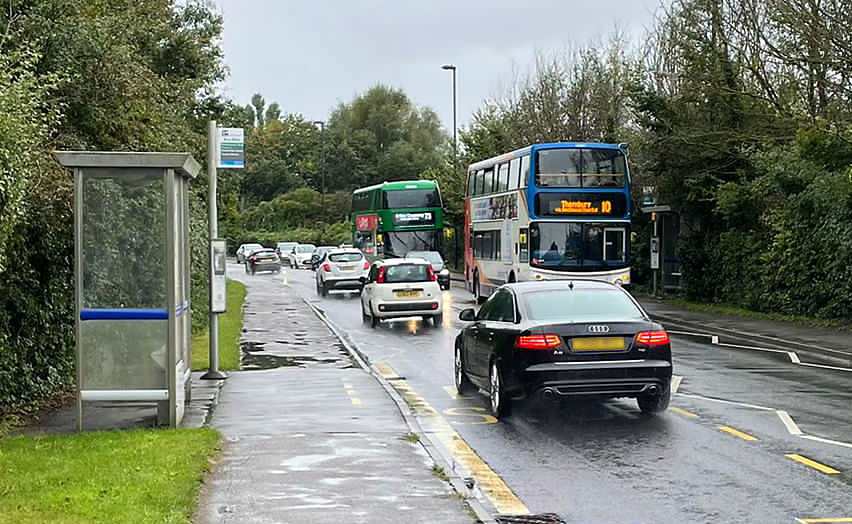 Photo of a bus waiting at a stop on a busy road.