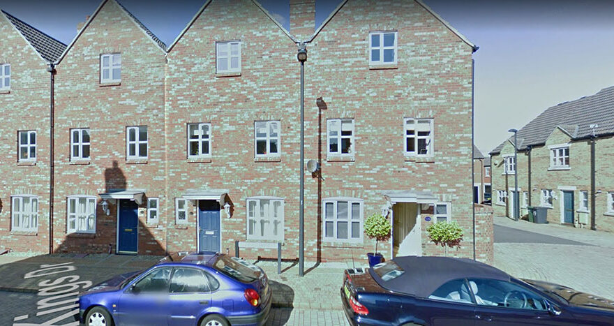 Photo of a row of terraced homes with car parks in front.