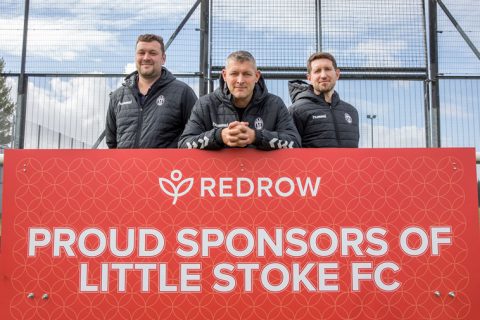 photo of three football players standing behind an advertising board.