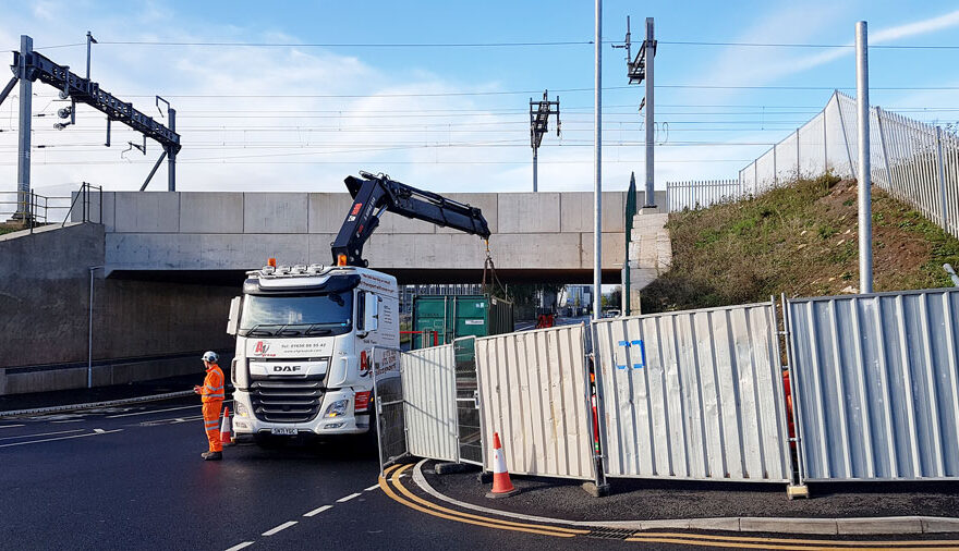 Photo of a lorry unloading a container close to a railway bridge.