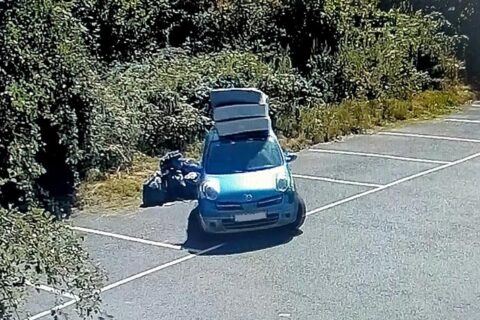 Photo of a car with mattresses on a roof rack and a number of black bin backs on the ground alongside it.