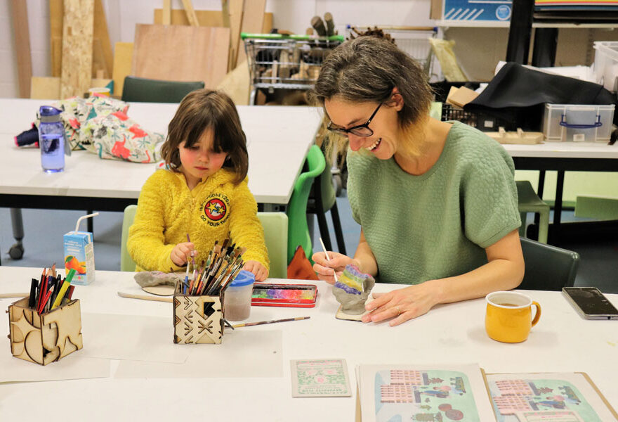 Photo of an adult and a child painting sculptures.