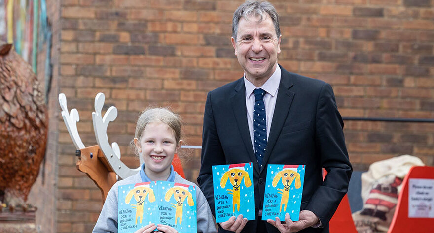 Photo of an adult and a child, both holding Christmas cards.