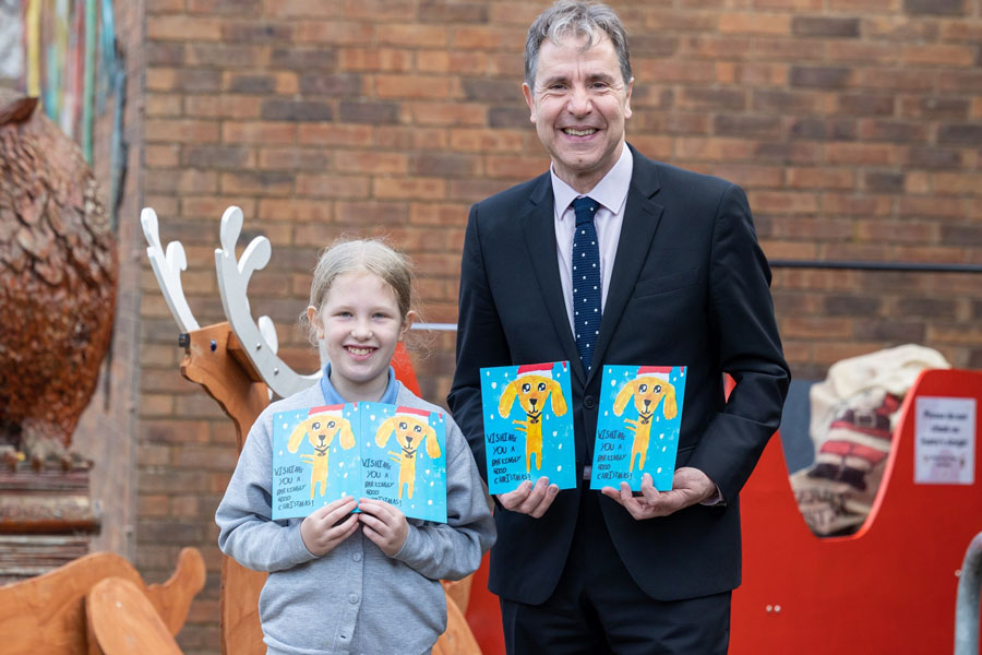 Photo of an adult and a child, both holding Christmas cards.